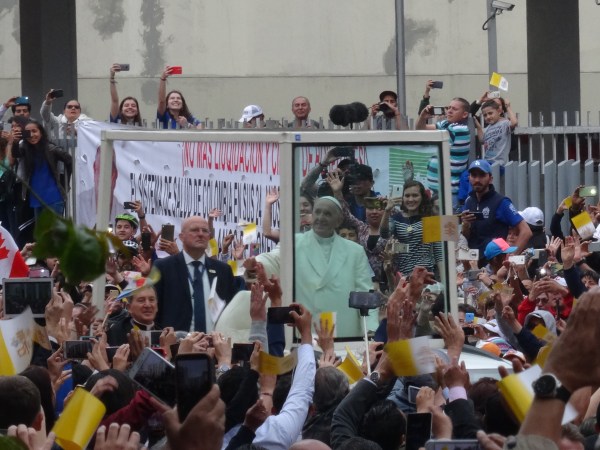 Pope in Popemobile with people surrounding him.