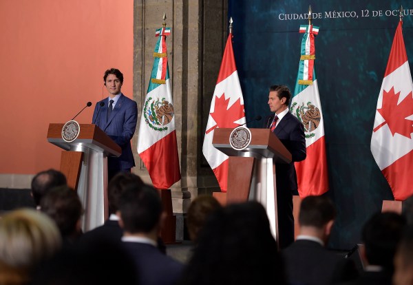 Two men stand at podiums with Mexican and Canadian flags behind them