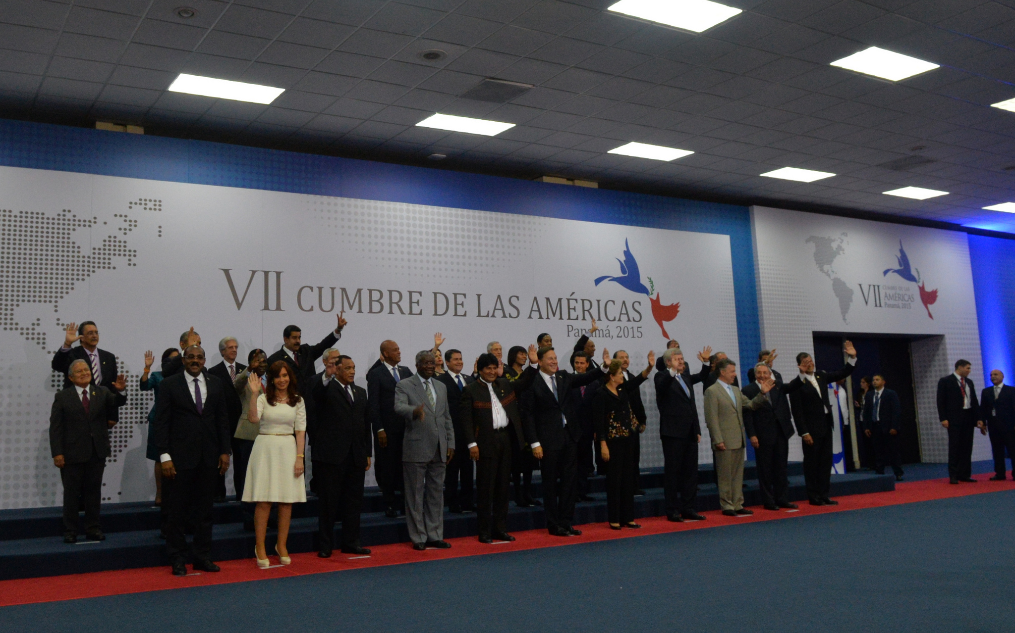 Large group of men and women stand awkwardly while waving to a crowd