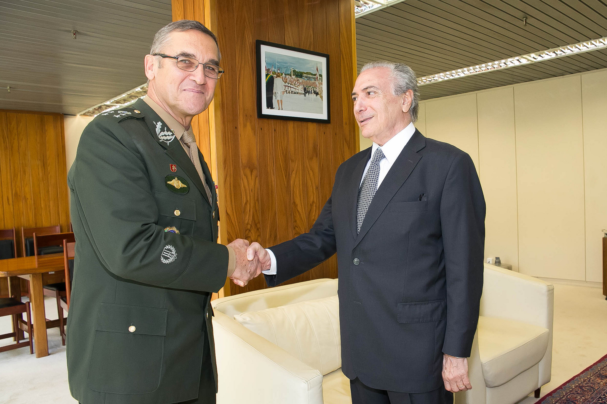 A man in a military uniform and a man in civilian dress shake hands