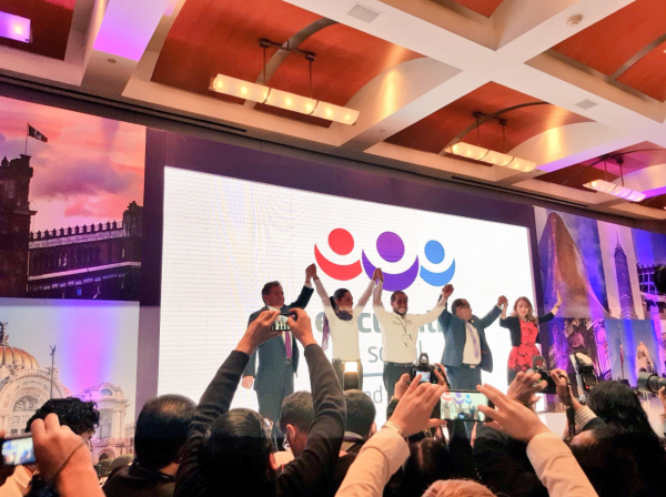 Five people stand up in front of a screen with their arms raised