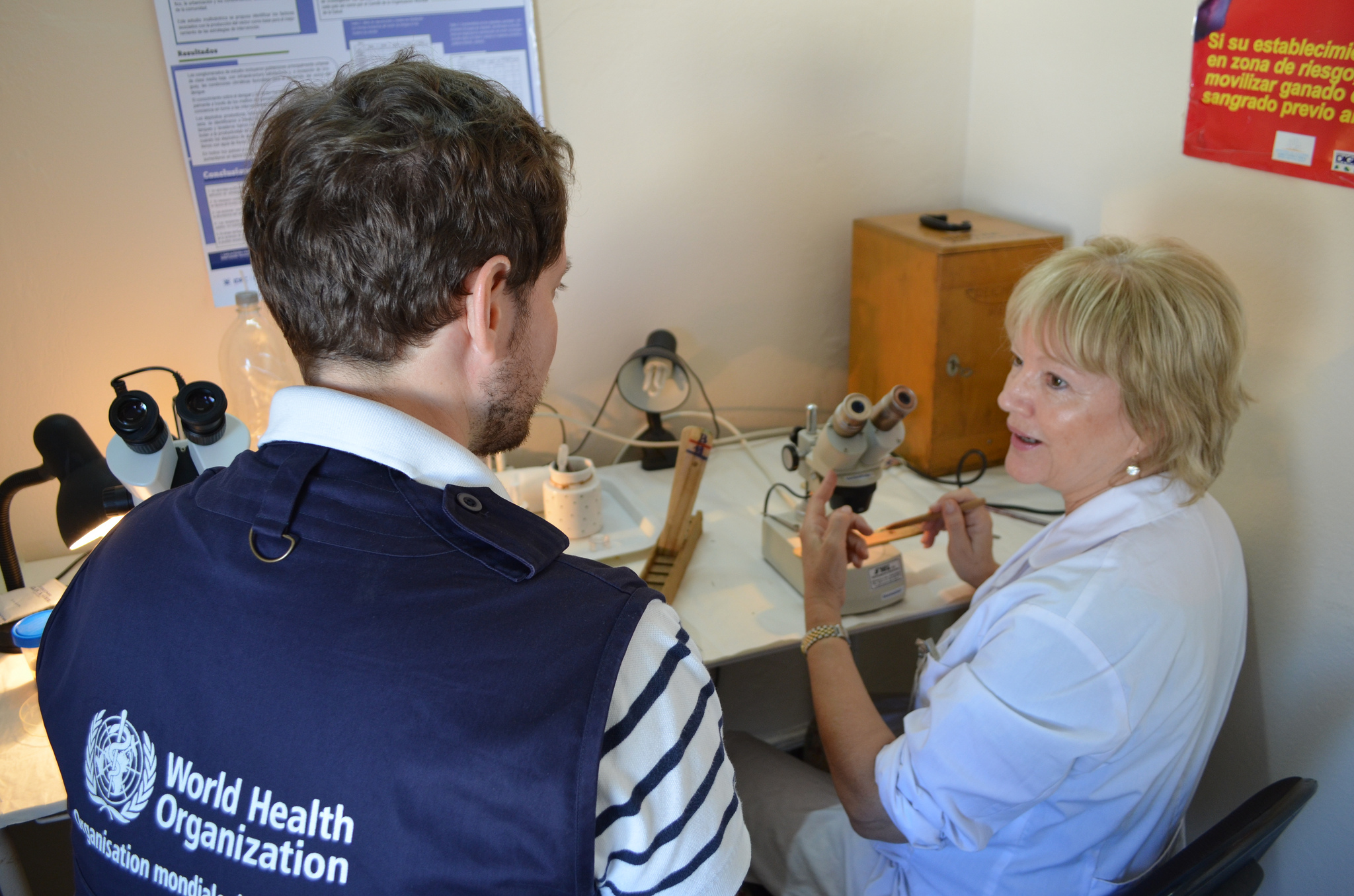 A woman points to a microscope while a man looks on.